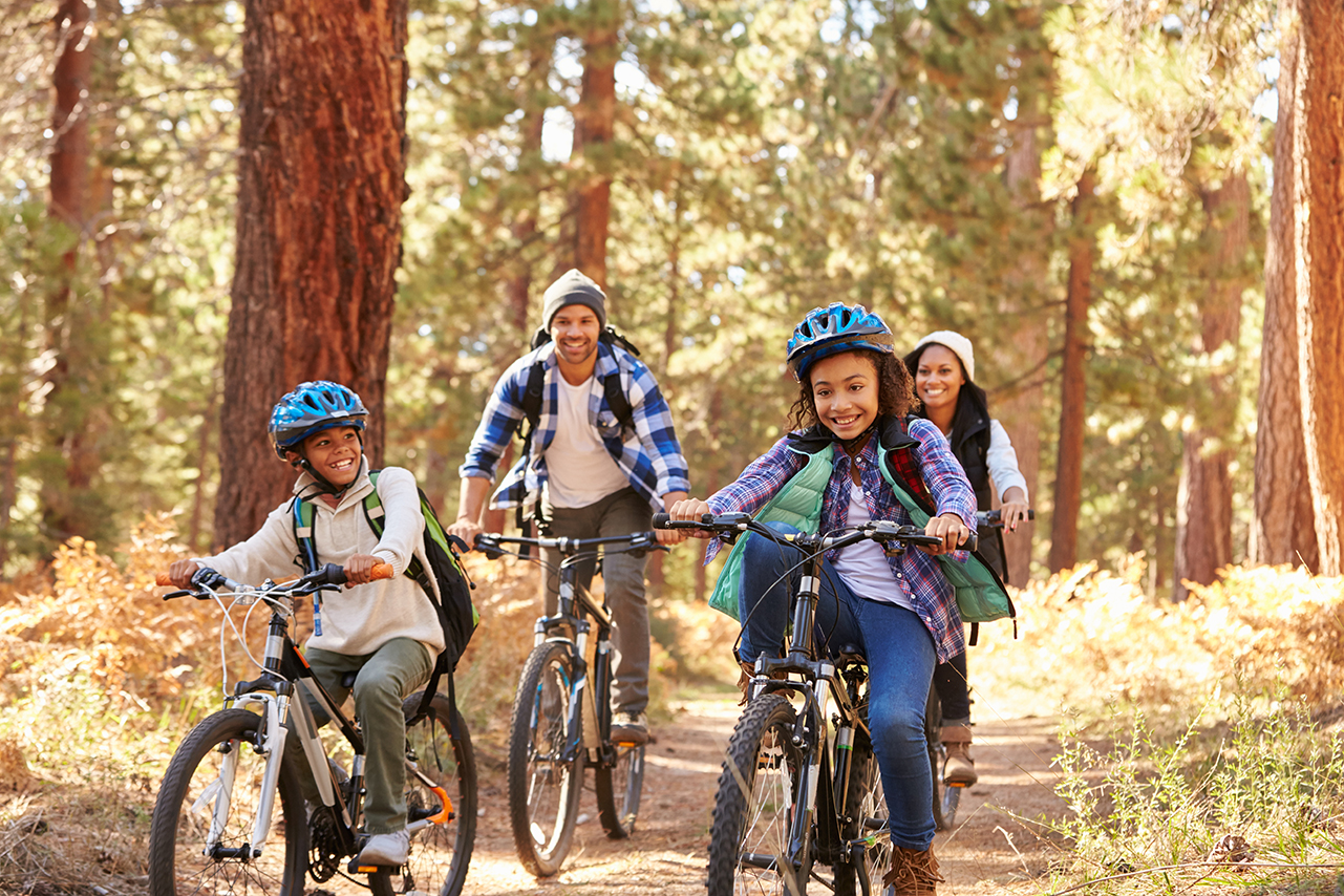 Family biking on a forest trail, smiling and wearing helmets
